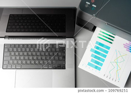 Modern printer with paper and laptop on table in office 109769251