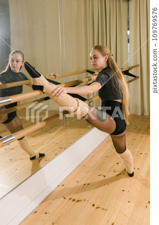 Young woman ballerina stretching and training at barre in dance studio - ballet and dancer concept 109769576