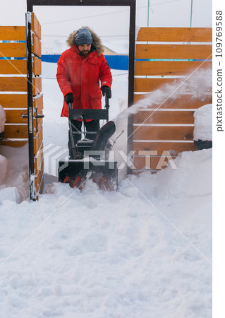 A man clear snow from backyard with snow blower. Winter season and snow blower equipment A man clear snow from backyard with snow blower. Winter season and snow blower equipment 109769588