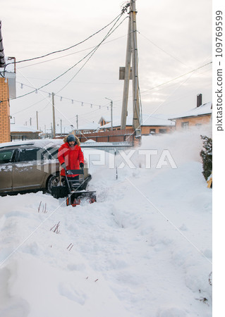 A man clear snow from backyard with snow blower. Winter season and snow blower equipment 109769599