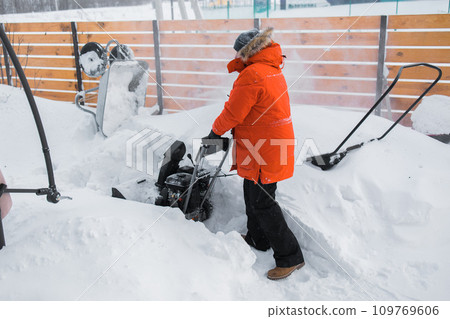 A man clear snow from backyard with snow blower. Winter season and snow blower equipment A man clear snow from backyard with snow blower. Winter season and snow blower equipment 109769606