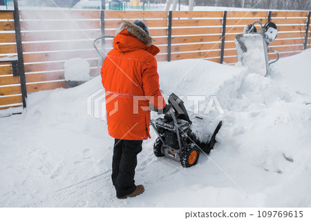 A man clear snow from backyard with snow blower. Winter season and snow blower equipment A man clear snow from backyard with snow blower. Winter season and snow blower equipment 109769615