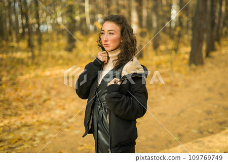 Attractive young woman walking in autumn park, happy mood and fashion style trend and curly long brown hair. Fall season and pretty female portrait copy space. Millennial generation concept 109769749