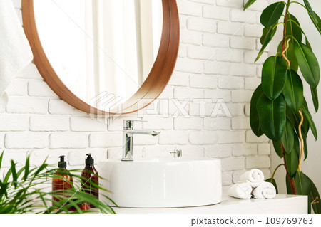 Bathroom interior with circle shaped mirror in wooden frame and white sink 109769763