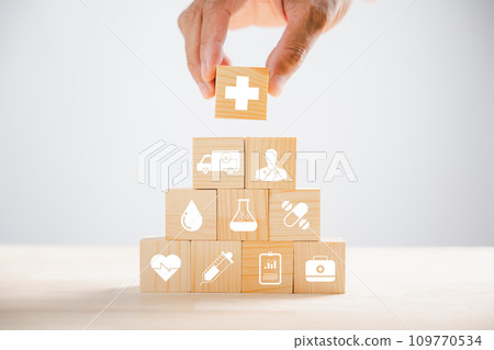 Hand holds wooden block with healthcare and medical icons, signifying safety, health, and family well-being. Illustrating pharmacy, heart care, and happiness concepts. health care concept Hand holds wooden block with healthcare and medical icons, signifying safety, health, and family well-being. Illustrating pharmacy, heart care, and happiness concepts. health care concept 109770534