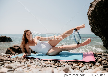 Woman sea fitness. Happy woman with long hair, fitness instructor in white bikini doing stretching and pilates on yoga mat near the sea. Female fitness yoga routine concept. Healthy lifestyle. 109771844
