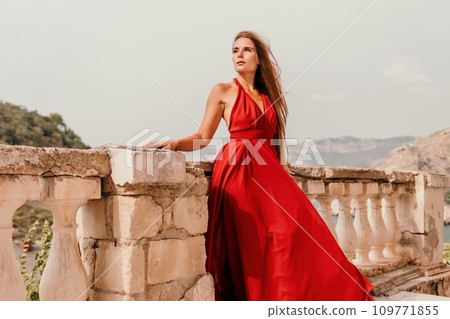 Woman travel portrait. Happy woman with long hair looking at camera and smiling. Close up portrait cute woman in a res long dress posing on backdrop of old travel city near sea Woman travel portrait. Happy woman with long hair looking at camera and smiling. Close up portrait cute woman in a res long dress posing on backdrop of old travel city near sea 109771855