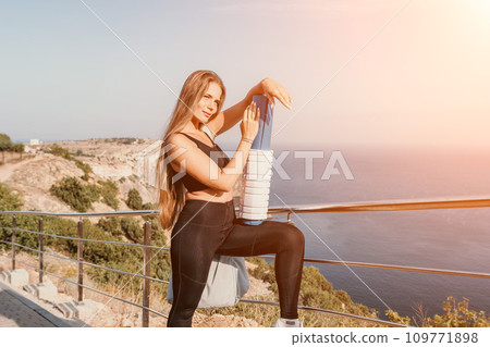 Fitness woman sea. Outdoor workout on yoga mat roller in park near to ocean beach. Female fitness pilates yoga routine concept. Healthy lifestyle. Happy fit woman exercising with rubber band in park. 109771898