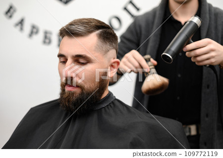 The hairdresser sweeps the hair during the haircut with a brush and drying air. The hairdresser sweeps the hair during the haircut with a brush and drying air. 109772119