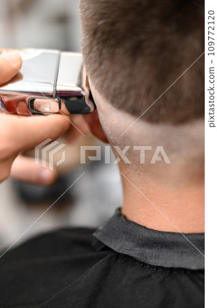 Barber shaves the temple with cordless trimmer during a short haircut on the sides of the head. 109772120