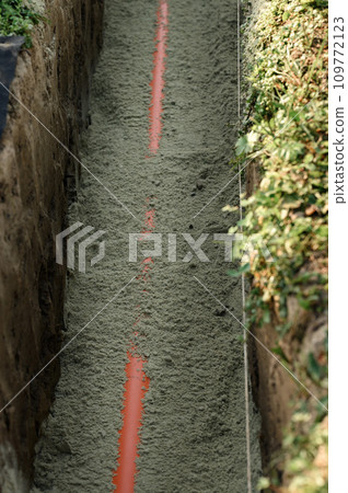 An orange reinforced sewer pipe is compacted with sand in a trench. Plumbing works on private plot. An orange reinforced sewer pipe is compacted with sand in a trench. Plumbing works on private plot. 109772123