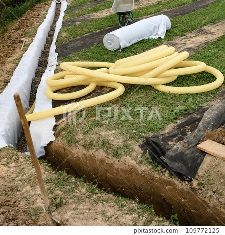 Yellow corrugated pipe with perforation in a trench with crushed stone and geotextile. Drainage works for the removal of ground water. 109772125