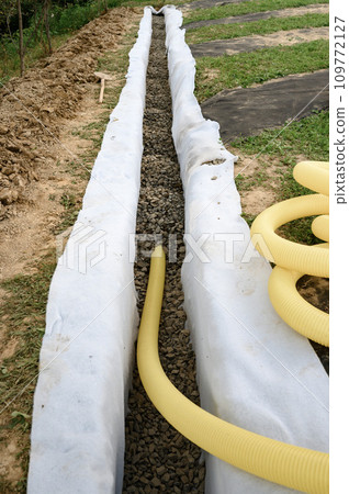 Yellow corrugated pipe with perforation in a trench with crushed stone and geotextile. Drainage works for the removal of ground water. 109772127