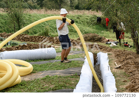 A worker carries a yellow perforated drainage pipe. Groundwater drainage works in the field 109772130