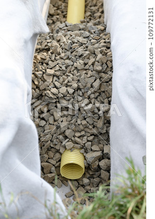 Yellow corrugated pipe with perforation in a trench with crushed stone and geotextile. Drainage works for the removal of ground water. 109772131