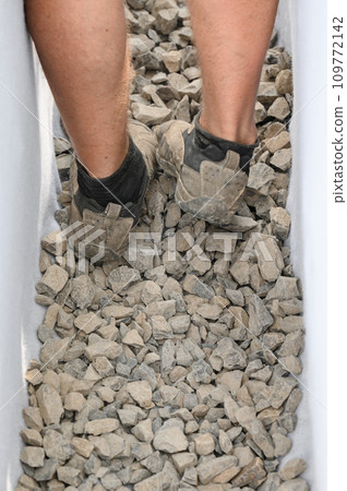 A worker stands in a drainage trench with white geotextile. Feet of the craftsman on the granite rubble closeup. 109772142