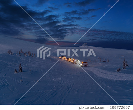 Snow groomers (snowcat ratrack machines) on night predawn excursion ride to winter mountain top with freeriders snowboarders. Alpine ski resort Dragobrat, Ukraine, Carpathian Mountains. Snow groomers (snowcat ratrack machines) on night predawn excursion ride to winter mountain top with freeriders snowboarders. Alpine ski resort Dragobrat, Ukraine, Carpathian Mountains. 109772697