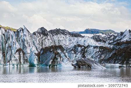 Solheimajokull picturesque glacier in southern Iceland. The tongue of this glacier slides from the volcano Katla. Beautiful glacial lake lagoon with blocks of ice and surrounding mountains. 109772743