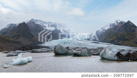 Glacier tongue slides from the Vatnajokull icecap or Vatna Glacier near subglacial Oraefajokull volcano, Iceland. Glacial lagoon with ice blocks and surrounding mountains. 109772897