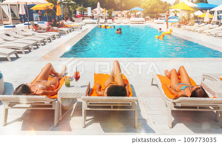 Group of friends relax on deck chair by the pool 109773035