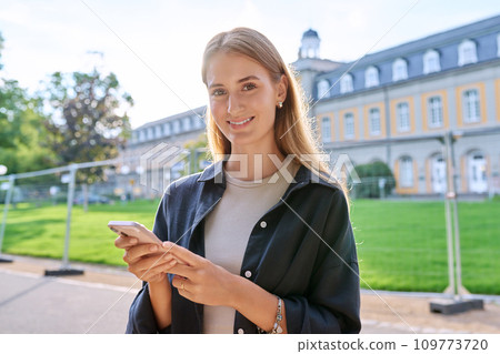 Young teenage female student using smartphone, looking at camera, outdoor Young teenage female student using smartphone, looking at camera, outdoor 109773720