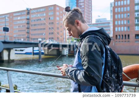 Fashionable young male with backpack using smartphone outdoors in city 109773739