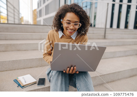 Smiling woman manager in eyeglasses is working on laptop sitting on background of office building 109775476