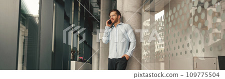 Smiling male sales manager talking phone with client while standing in coworking and looking at side Smiling male sales manager talking phone with client while standing in coworking and looking at side 109775504