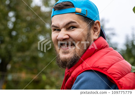 A man with a dubious expression, his features distorted into a funny grimace, is captured in nature as he looks into the camera. 109775779