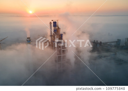 Aerial view of cement factory with high concrete plant structure and tower crane at industrial manufacturing site on foggy evening. Production and global industry concept. Aerial view of cement factory with high concrete plant structure and tower crane at industrial manufacturing site on foggy evening. Production and global industry concept. 109775848