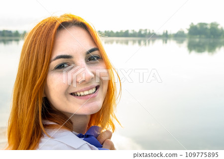 Portrait of happy smiling red haired girl. Positive young woman looking in camera outdoors. 109775895