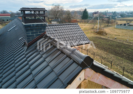 Closeup of house roof top covered with ceramic shingles. Tiled covering of building under construction Closeup of house roof top covered with ceramic shingles. Tiled covering of building under construction 109775977