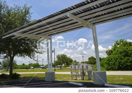 Solar panels installed as shade roof over parking lot for parked electric cars for effective generation of clean electricity. Photovoltaic technology integrated in urban infrastructure 109776022