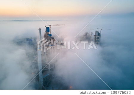 Aerial view of cement factory with high concrete plant structure and tower crane at industrial manufacturing site on foggy evening. Production and global industry concept. 109776023