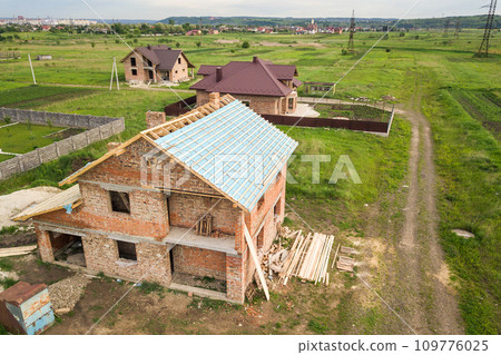 Aerial view of a brick house with wooden roof frame under construction. 109776025