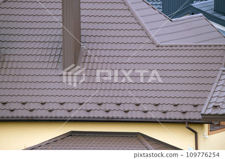 Snow guard for safety in winter on house roof top covered with steel shingles. Tiled covering of building Snow guard for safety in winter on house roof top covered with steel shingles. Tiled covering of building 109776254
