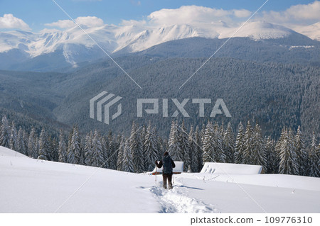 Man backpacker hiking snowy mountain hillside on cold winter day. 109776310