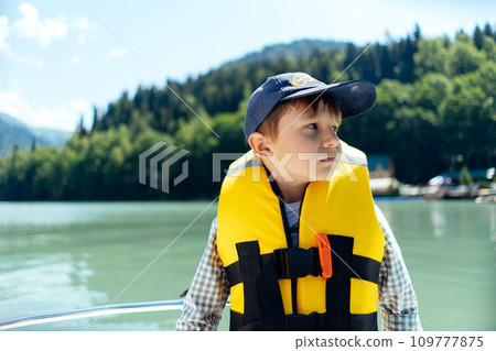boy wearing safety vest feel sick sailing paddleboat on beautiful Lake. mountains on background boy wearing safety vest feel sick sailing paddleboat on beautiful Lake. mountains on background 109777875