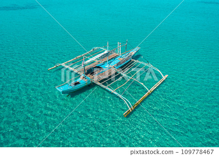 Aerial drone view of traditional philippine boat bangka anchored in the bay with clear and turquoise water on sunny day. Boat in the tropical lagoon. El Nido, Palawan island, Philippines. Aerial drone view of traditional philippine boat bangka anchored in the bay with clear and turquoise water on sunny day. Boat in the tropical lagoon. El Nido, Palawan island, Philippines. 109778467