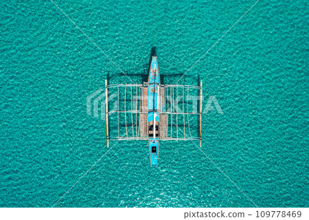 Aerial drone view of traditional philippine boat bangka anchored in the bay with clear and turquoise water on sunny day. Boat in the tropical lagoon. El Nido, Palawan island, Philippines. Aerial drone view of traditional philippine boat bangka anchored in the bay with clear and turquoise water on sunny day. Boat in the tropical lagoon. El Nido, Palawan island, Philippines. 109778469