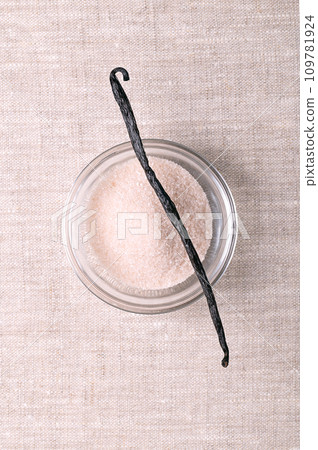 Vanilla bean and vanilla sugar, in glass bowl, over linen. Dried, whole, brown, ripe fruit of Vanilla planifolia. Spice with distinctive flavor, placed over bowl with flavored sugar, used for baking. Vanilla bean and vanilla sugar, in glass bowl, over linen. Dried, whole, brown, ripe fruit of Vanilla planifolia. Spice with distinctive flavor, placed over bowl with flavored sugar, used for baking. 109781924