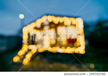 Abstract defocused bright Christmas lights on wooden house, creating decorative illumination in evening scene Abstract defocused bright Christmas lights on wooden house, creating decorative illumination in evening scene 109782590