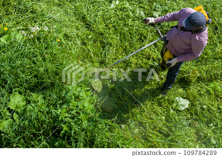 lawnmower man with string trimmer trimming grass at sunny day lawnmower man with string trimmer trimming grass at sunny day 109784289