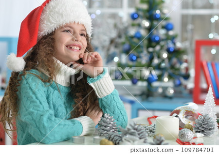 Happy girl in Santa hat sitting with Christmas present Happy girl in Santa hat sitting with Christmas present 109784701