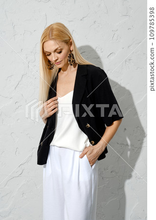 Blonde woman in loose black jacket and loose trousers looking down Blonde woman in loose black jacket and loose trousers looking down 109785398