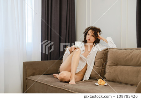 Romantic and dreamy lonely woman sitting on sofa with cup of cappuccino on her knee Romantic and dreamy lonely woman sitting on sofa with cup of cappuccino on her knee 109785426