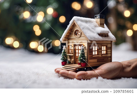 A realistic wooden modern tiny house in a small size in Christmas decor and snow, on the palm of hand. Festive mood and comfort, gift, mortgage, housing, rent, moving in New Year. Copy space 109785601
