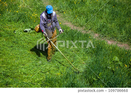 lawnmower man with string trimmer trimming grass at sunny day lawnmower man with string trimmer trimming grass at sunny day 109786668