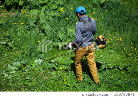 lawnmower man with string trimmer trimming grass at sunny day lawnmower man with string trimmer trimming grass at sunny day 109786671