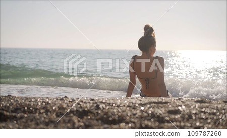 The girl in a bathing suit sunbathes on the seashore. Girl in a bathing suit lies on the seashore and relaxes. Waves caress the girl's body. The girl in a bathing suit sunbathes on the seashore. Girl in a bathing suit lies on the seashore and relaxes. Waves caress the girl's body. 109787260